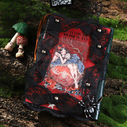 A gothic-style journal or notebook with a black lace cover, red decorative paper, silver nail studs, and a spider embellishment, photographed outdoors on mossy wood with small mushrooms nearby.