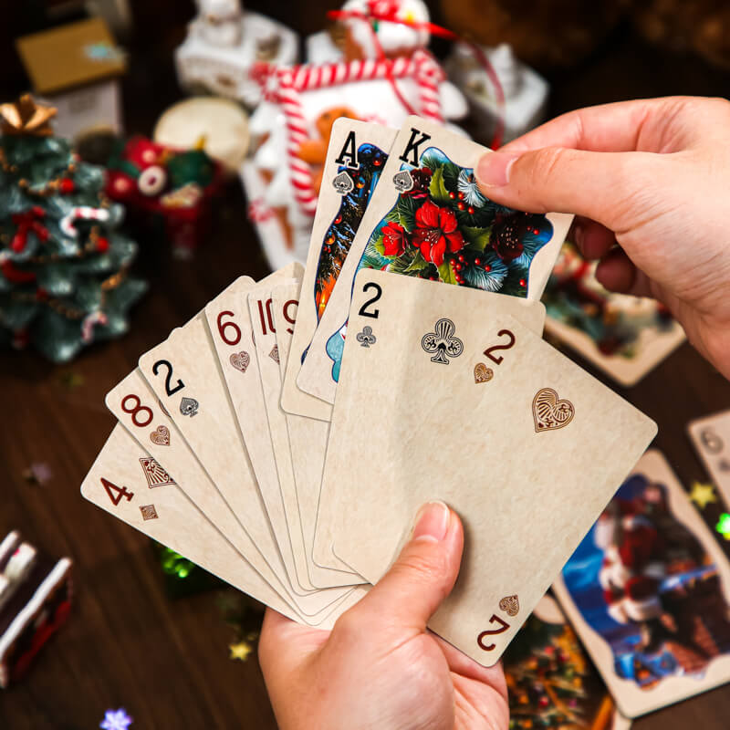 HandsdisplayingChristmasplayingcardswithpoinsettiaartworkandvintagenumberedsuits