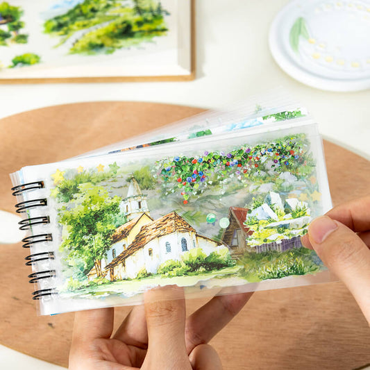 HandsholdingaclearPETstickersheetfeaturingacountrysidecottageandfloweringgreenery