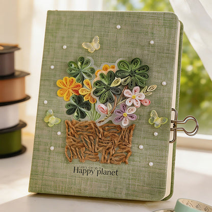 A green textured hardcover notebook with 3D quilled flowers, butterflies, and a paper basket design on the cover, featuring a metal binder clip on the side and the text 'Happy planet' near the bottom.