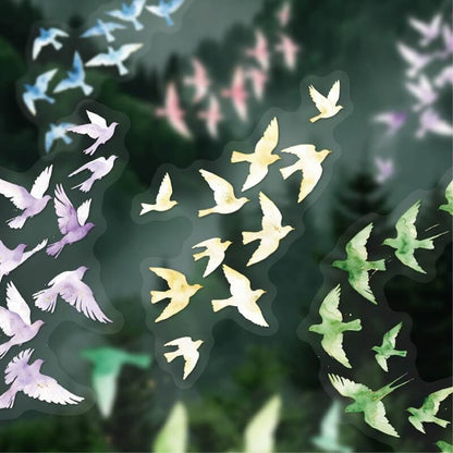 A sheet of die-cut stickers featuring watercolor-style birds in soft pastel colors including yellow, green, lavender, and light blue, set against a blurred dark forest background.